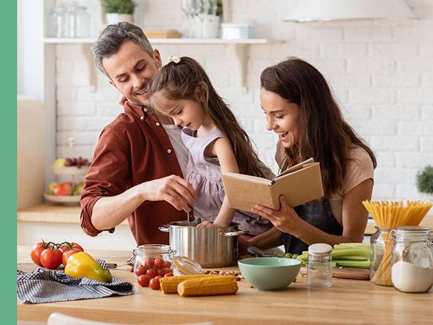 Familie kocht zusammen: Pasta, Gemüse und Kochbuch.