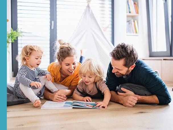 Familie liest ein Kinderbuch auf dem Boden.