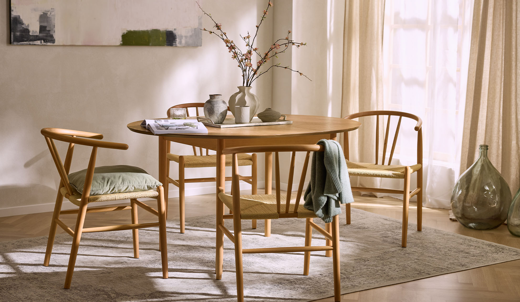 Helles Esszimmer mit rundem Holztisch, Holzstühlen mit Seilsitzen und Blumendekoration.