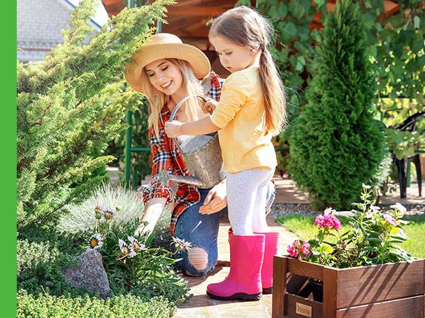 Mutter und Tochter im Garten beim Gießen, rosa Gummistiefel.