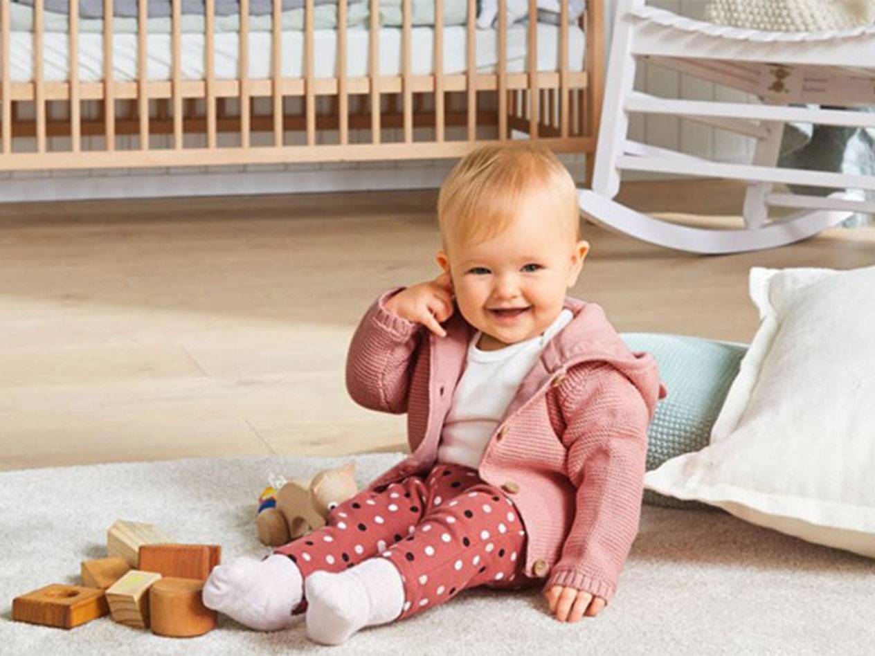 Baby in rosa Strickjacke und Leggings spielt mit Holzspielzeug.
