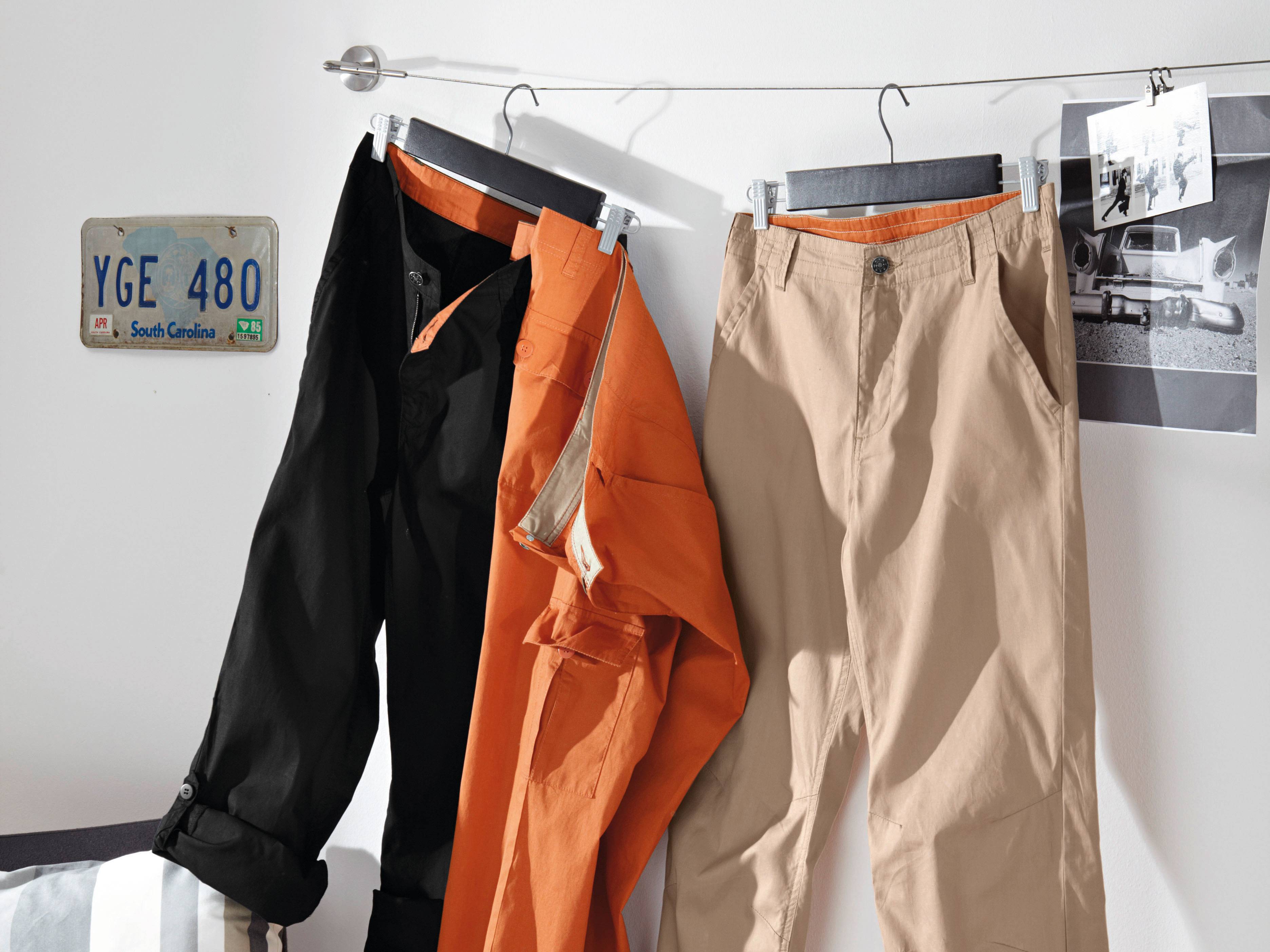 Beige und schwarze Hosen sowie eine orange Jacke an einem Kleiderbügel.