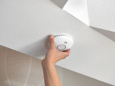 Eine Hand montiert einen weißen Rauchmelder an der Decke.