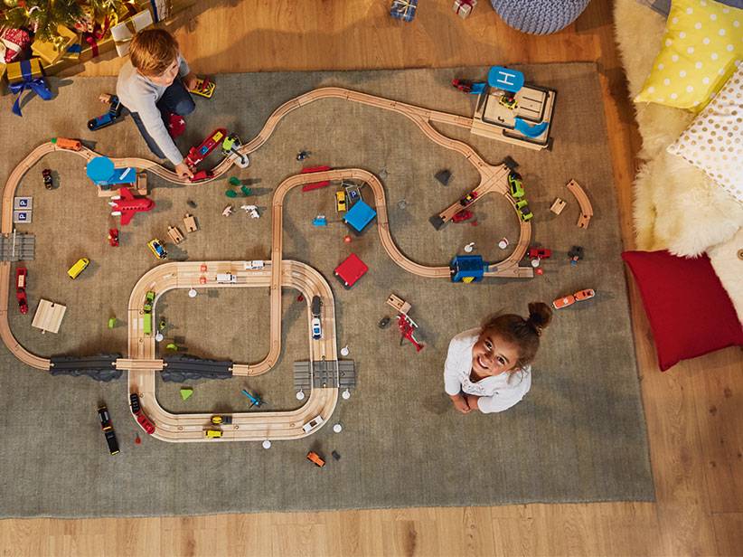 Kinder spielen mit Holzeisenbahn und Autos.
