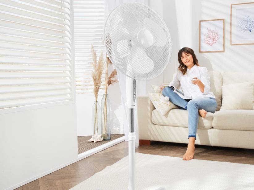 Weißer Standventilator und entspannte Frau auf Sofa.