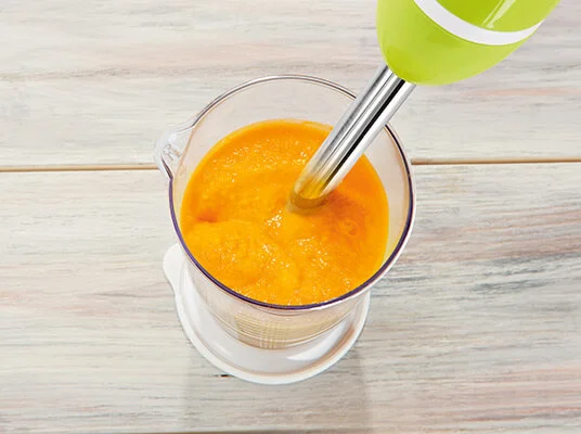 Pürierte Suppe wird mit einem Stabmixer bearbeitet.