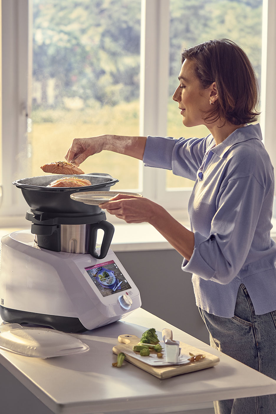Frau bereitet Lachs und Gemüse mit einer multifunktionalen Küchenmaschine zu.