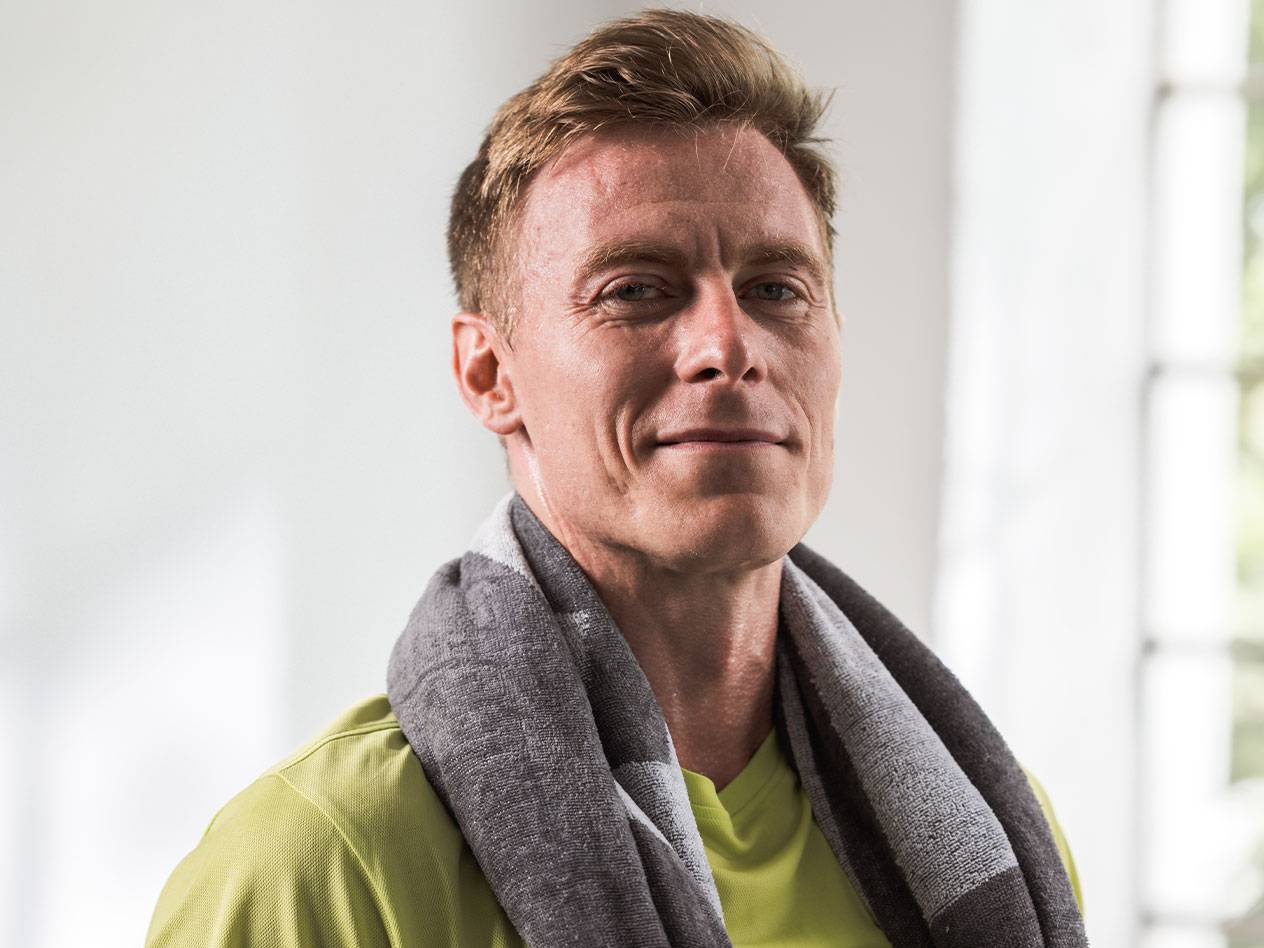 Ein blonder Mann mit einem Handtuch um den Hals blickt in die Kamera.