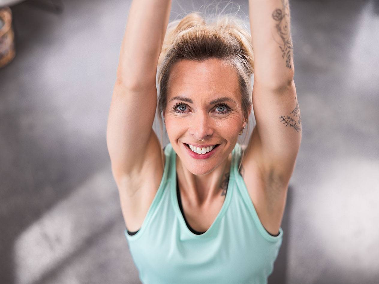 Blonde Frau in hellblauem Tanktop lächelt in die Kamera.