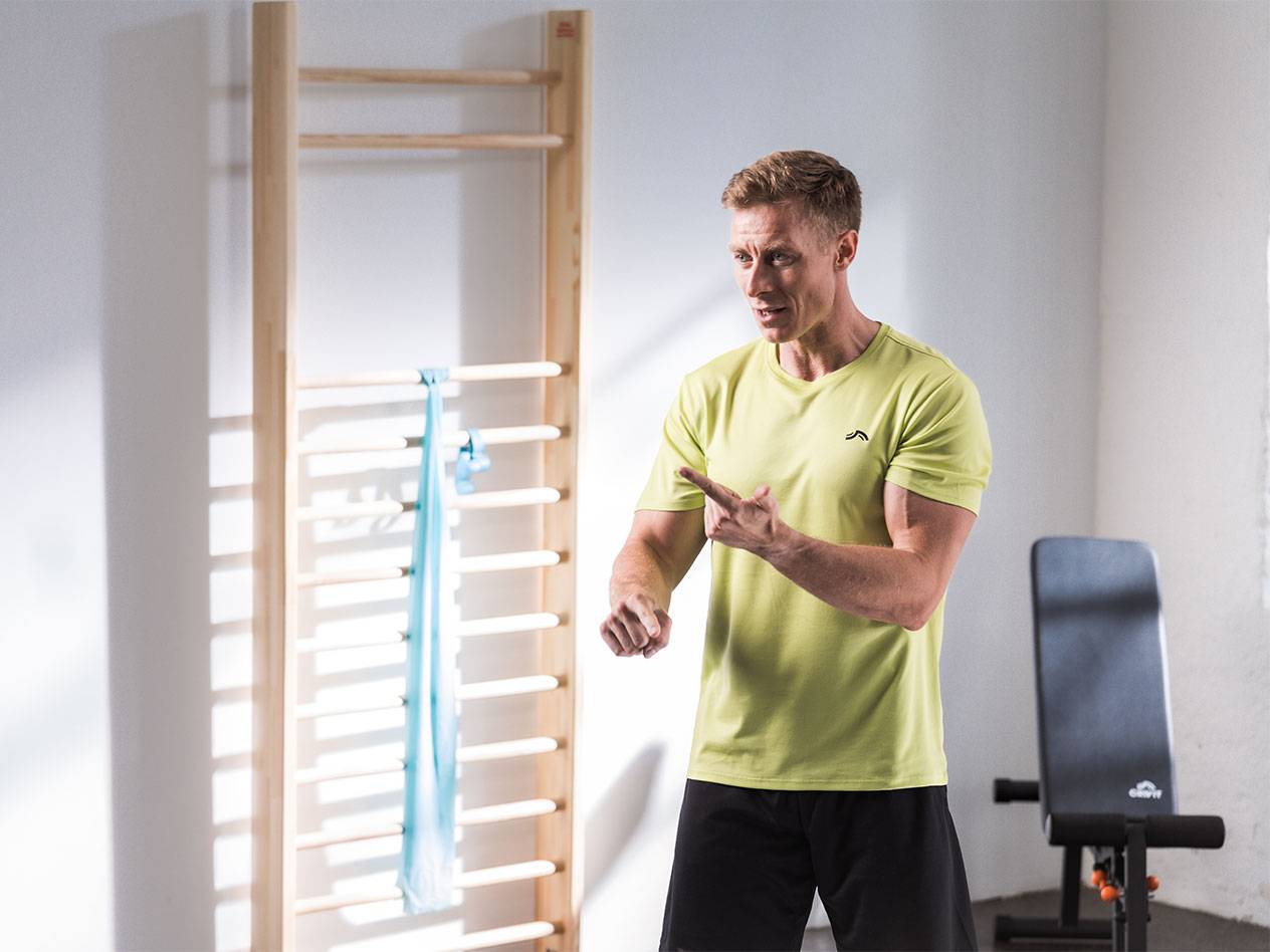 Ein Mann in Sportkleidung steht vor einer Sprossenwand mit einem Widerstandsband.