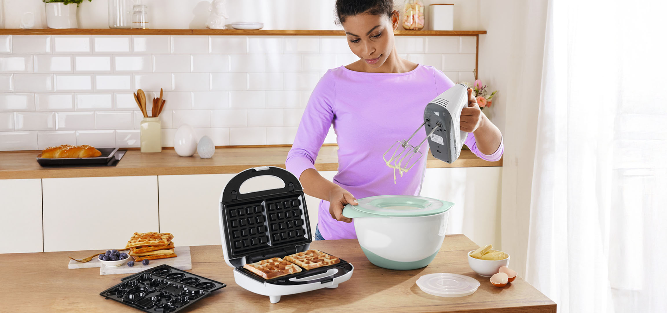 Frau bereitet Waffeln und Donuts mit einem Waffeleisen und Handmixer zu.