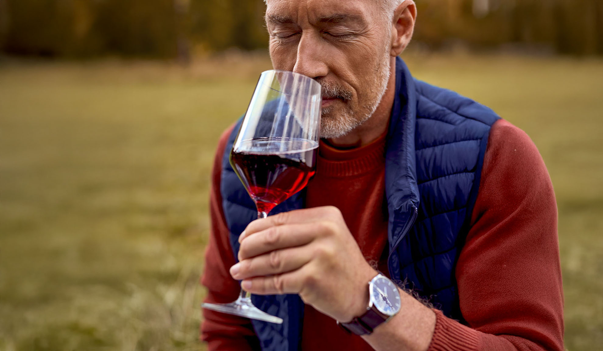 Bärtiger Mann riecht im Freien an einem Glas Rotwein.