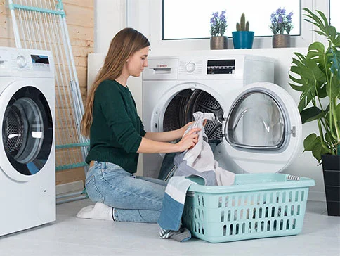 Frau sortiert Wäsche in Waschmaschine, Trockner und Korb.