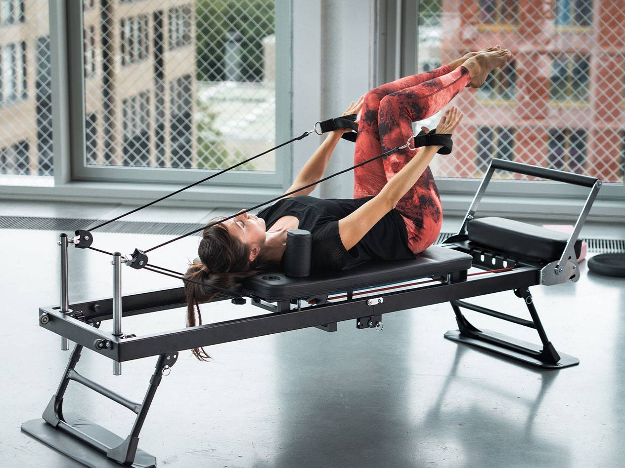Frau macht Pilates auf einem Reformer in roter Yogahose.