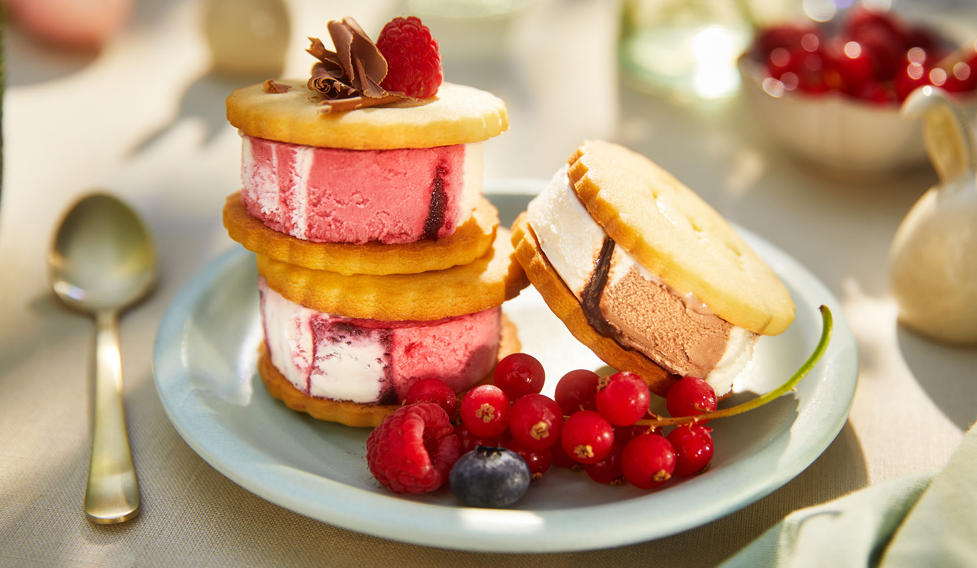 Eis-Sandwiches mit Beeren auf einem hellblauen Teller in sonniger Außenumgebung.