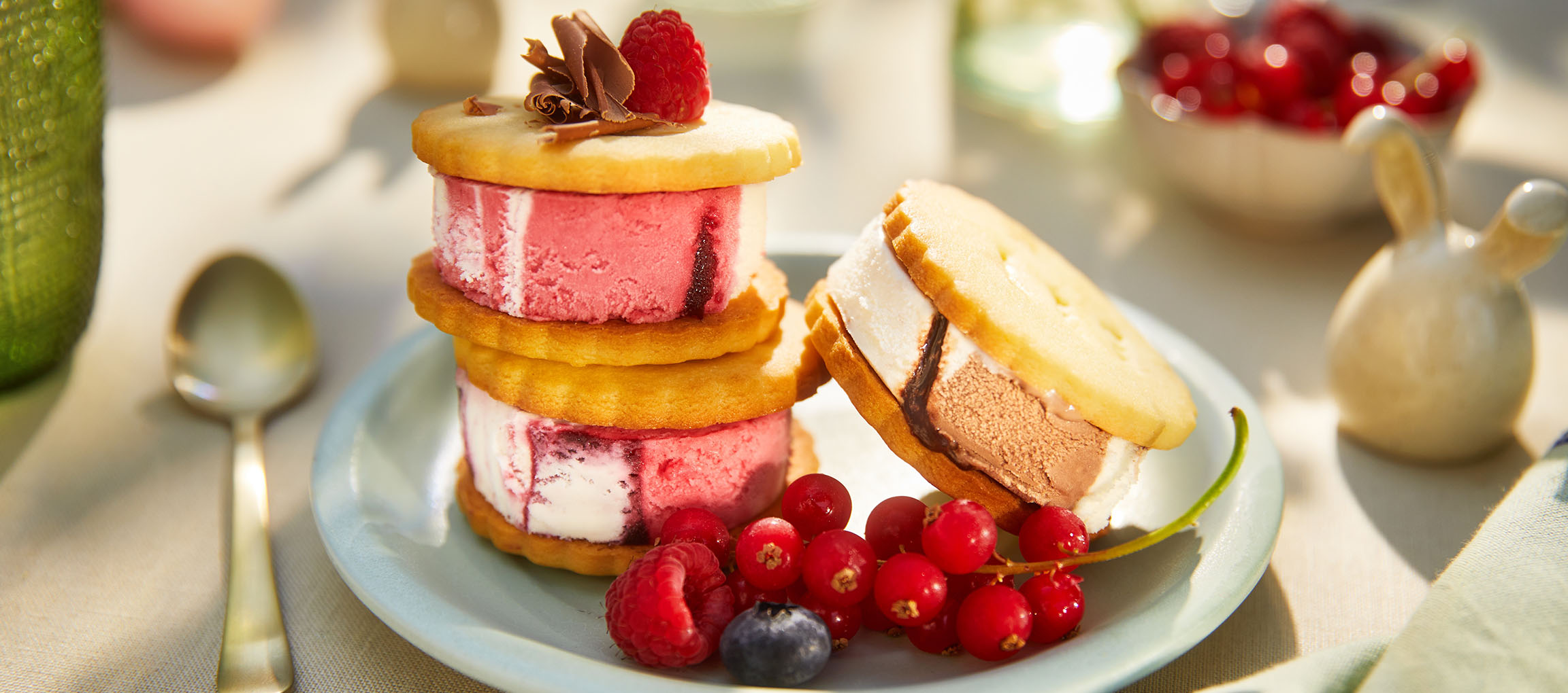 Eis-Sandwiches mit Beeren auf einem hellblauen Teller in sonniger Außenumgebung.