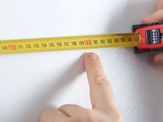 Gelbes Maßband und Finger auf weißem Hintergrund.