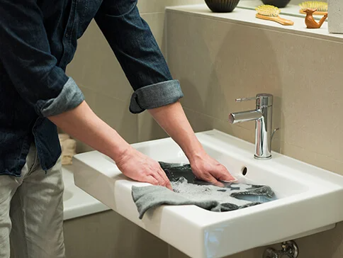 Mann wäscht dunkle Kleidung und Stoff im Waschbecken.