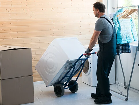 Ein Mann transportiert eine Waschmaschine und andere Güter auf einem Handwagen.