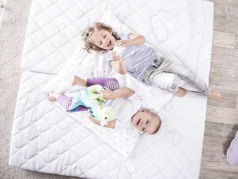 Kinder spielen auf einer weichen Spielmatte mit Plüschtieren.