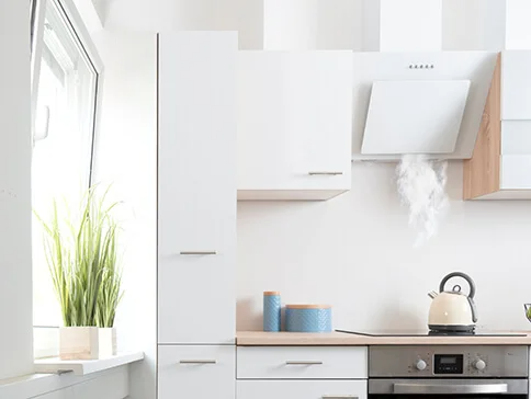 Weiße Dunstabzugshaube und Küchenschränke über kochendem Wasserkessel.