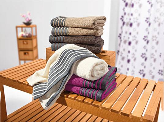 Badetextilien: gestreifte und unifarbene Handtücher auf einer Holzbank.