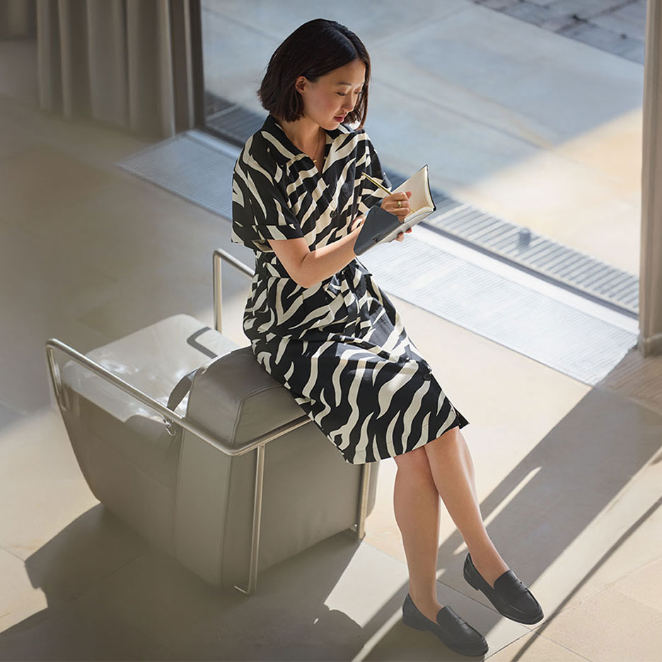 Frau in einem Zebra-Kleid und Loafern, die in ein Notizbuch schreibt.
