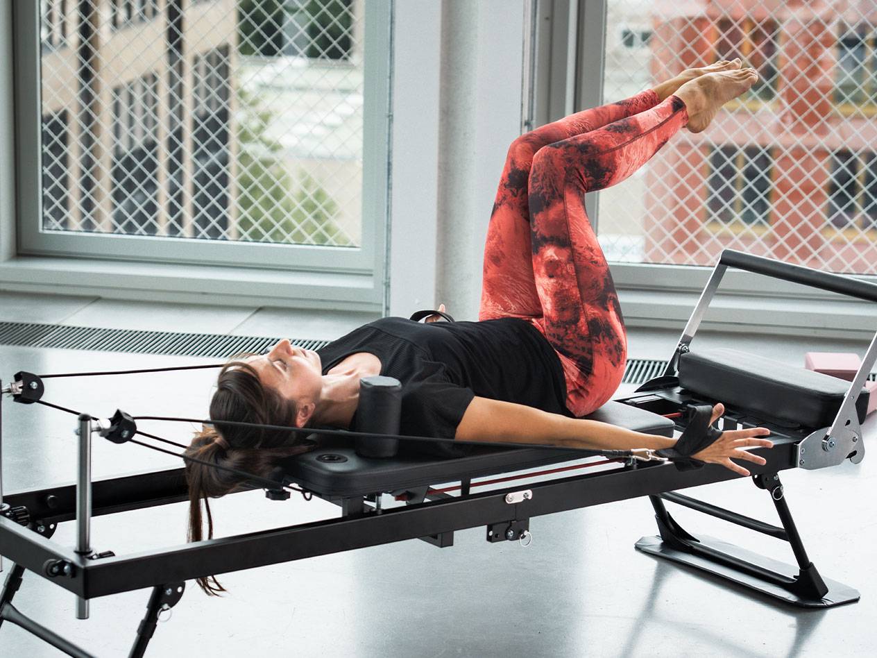 Frau macht Pilates auf einem Reformer, in rot-schwarzen Leggings