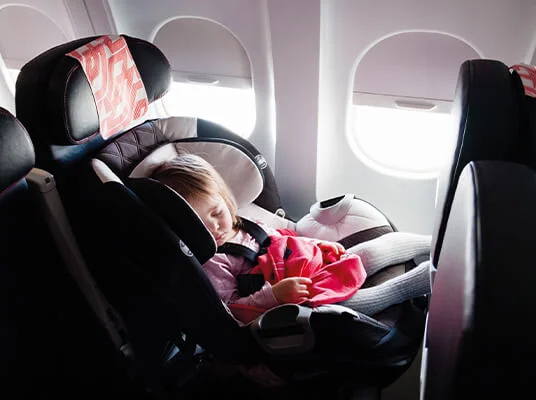 Kind schläft in einem Kindersitz im Flugzeug.