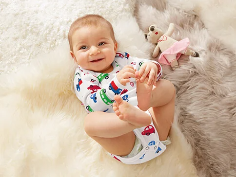 Baby in Auto-Bodysuit und Spielzeug.
