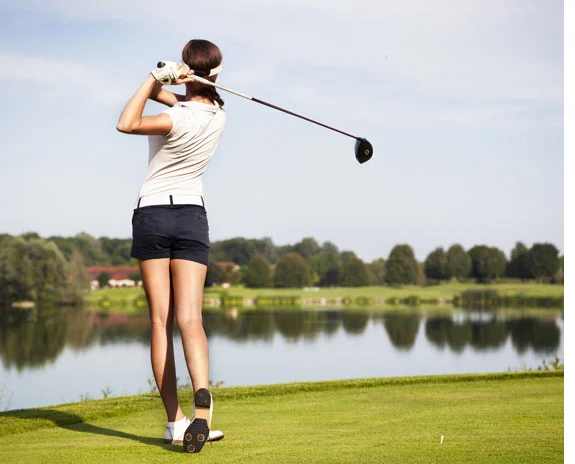 Golferin beim Abschlag am See.