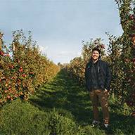 Mann steht inmitten von Apfelbäumen mit reifen Äpfeln.