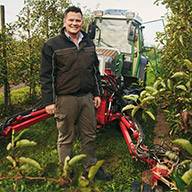 Bauer mit Fendt-Traktor und Anbaugerät in Apfelplantage.