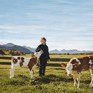 Bäuerin mit zwei jungen Braunvieh-Kälbern auf einer Weide.