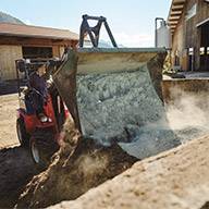 Ein Landwirt verwendet einen kompakten Hoflader zum Abladen von Material.