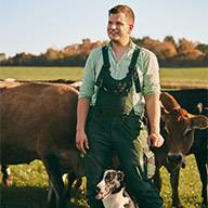 Junger Landwirt mit Kühen und Hund auf der Weide.