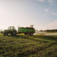Ein grüner Traktor mit Anhänger verteilt organischen Dünger auf einem Feld.