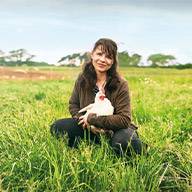 Frau hält ein weißes Huhn auf einem grünen Feld.