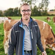Lächelnder Landwirt vor seinen Kühen auf einer Weide.