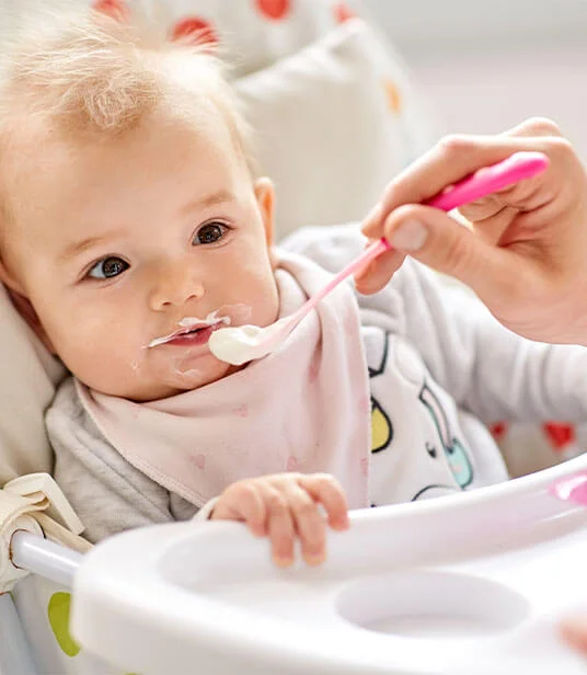 Baby isst Joghurt im Hochstuhl.