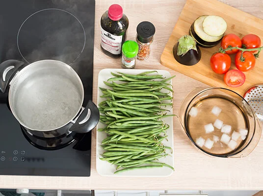 Grüne Bohnen, Tomaten, Auberginen und kochendes Wasser im Topf.