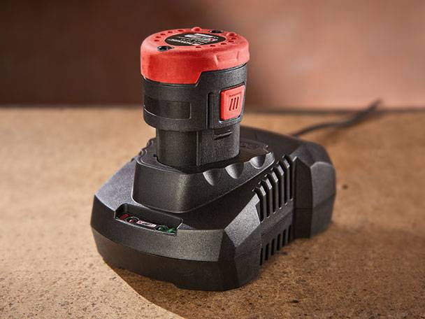 Akku und Ladegerät: Roter Akku, schwarzes Ladegerät.