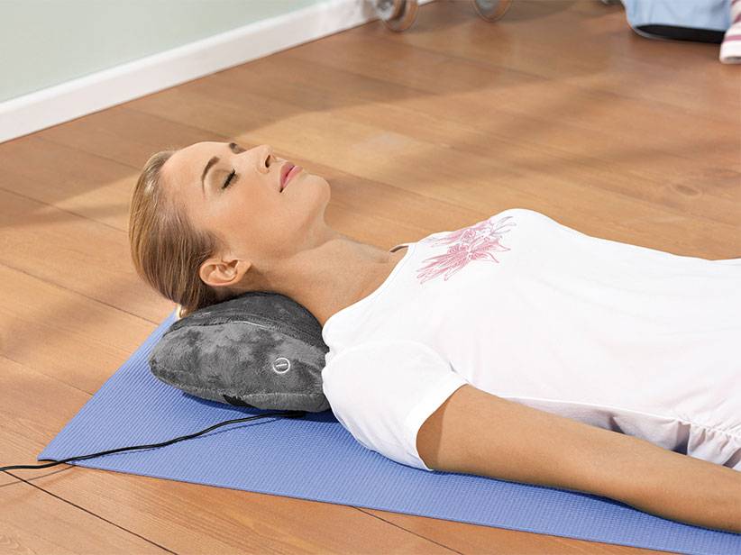 Frau entspannt sich mit Massagekissen auf Yogamatte.