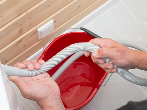 Wasser wird mit einem Schlauch aus einer Waschmaschine in einen Eimer geleert.