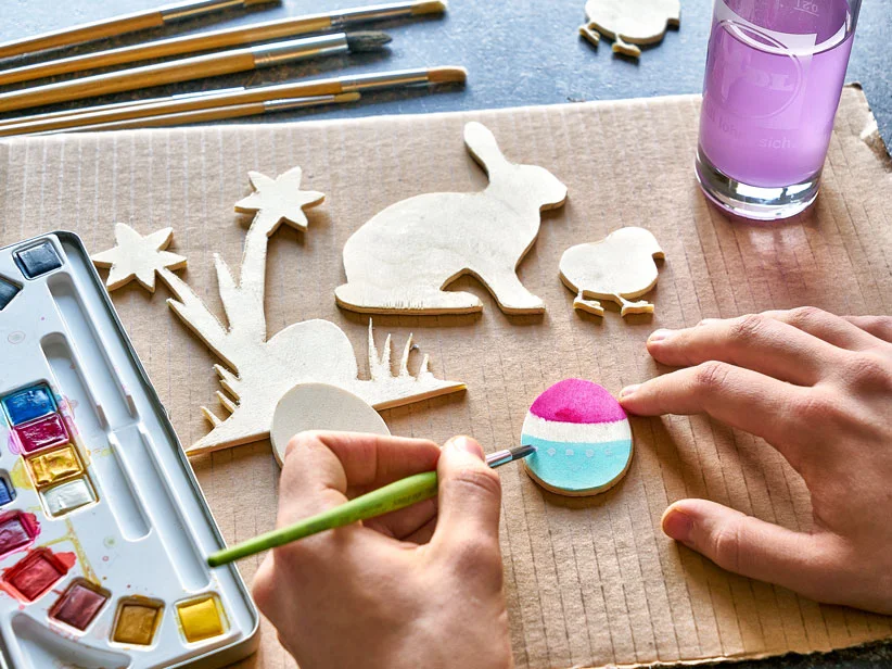Bemalen von hölzernen Ostereiern und -dekorationen mit Wasserfarben.