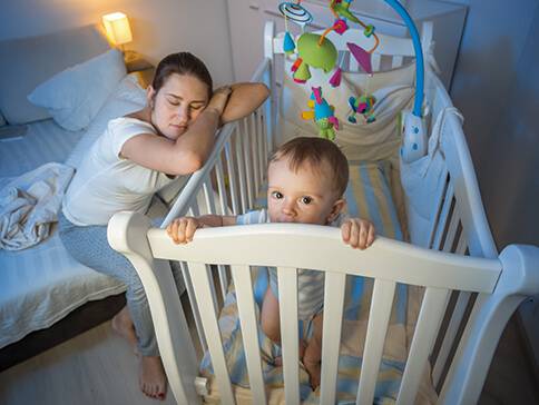 Mutter schläft neben dem Baby im Gitterbett.