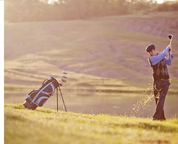 Golfer schlägt Ball, Schläger und Tasche im Gras.