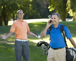 Zwei Golfer auf dem Platz, einer telefoniert.