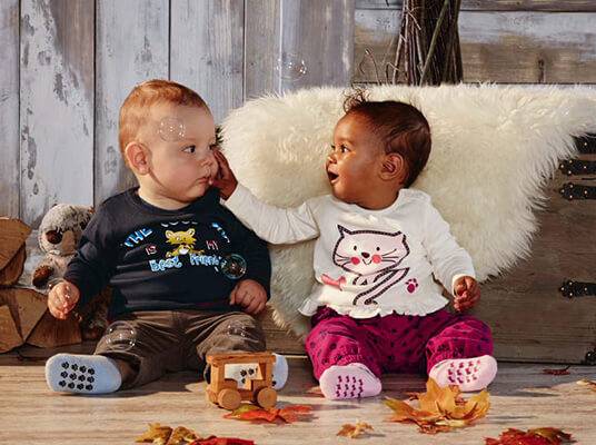 Zwei Babys in süßen Outfits: ein Junge mit einem Katzenmotiv-Shirt und ein Mädchen in niedlichen Katzen-Klamotten.