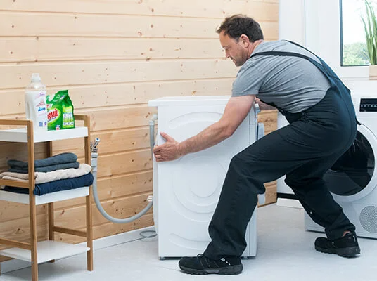 Mann bewegt Waschmaschine und Trockner in der Waschküche.